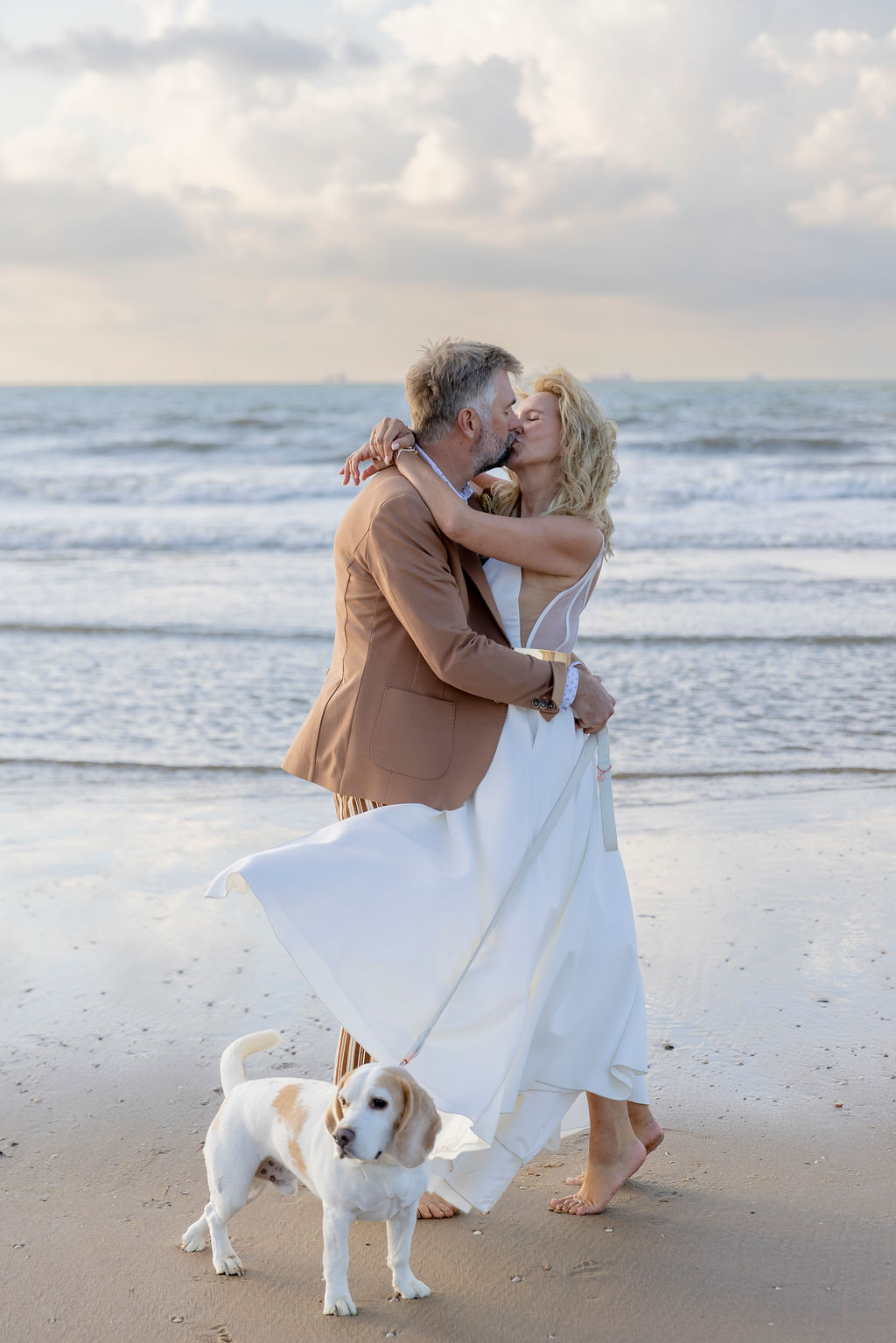 ein Silberhochzeit Brautpaar knutscht am Strand, während der Familienhund daneben steht | Hochzeitsplanung: Sagt Ja