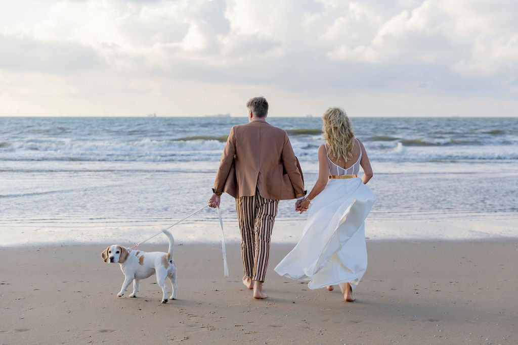 beim Paarshooting am Strand läuft das Silberhochzeit Paar mit seinem Hund aufs Meer zu | Hochzeitsplanung: Sagt Ja